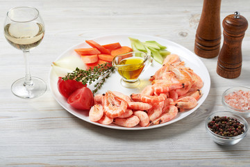 The ingredients for shrimp bisque sauce are on a white plate. Shrimp, tomatoes, onions, carrots, celery, thyme, oil, salt, pepper, white wine.