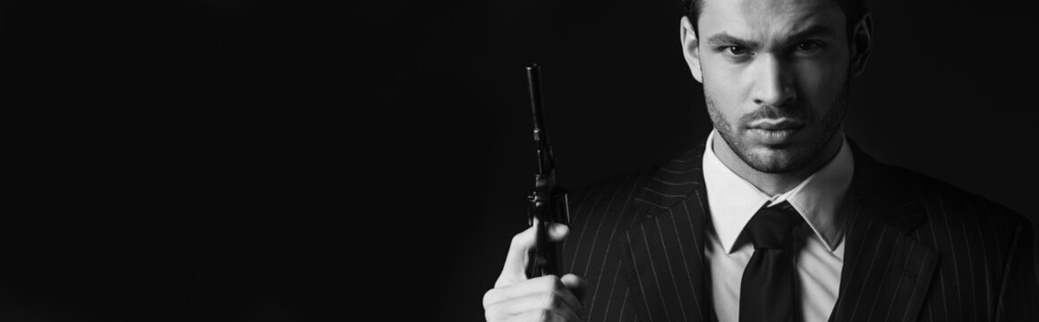 Monochrome image of gangster holding gun and looking at camera isolated on black, panoramic  shot