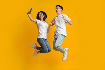Fototapeta na wymiar Crazy asian couple jumping and taking selfie on smartphone