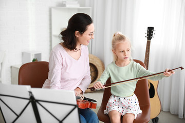 Private music teacher giving violin lessons to little girl at home