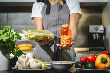 Close up of female hands holding celery and nutritional supplements or vitamins in the kitchen. Choice, balanced diet and health concept.
