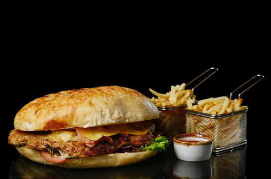 big fresh beef burger with cheese, tomatoes, onion and French fries. isolated on black background.