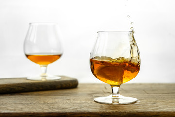 Cognac \ whiskey in cognac glass on wooden table, golden color spirits splashing on white background