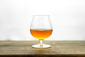 Cognac \ whiskey in cognac glass on wooden table, golden color spirits splashing on white background