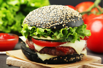 A black burger with vegetables and beef meat
