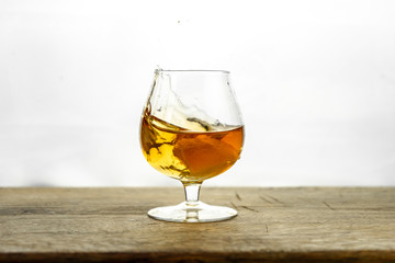 Cognac \ whiskey in cognac glass on wooden table, golden color spirits splashing on white background