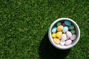 Chocolate Easter eggs glazed with pastel coloring in a bowl over green grass background. Happy Easter concept. Copy space. Top view