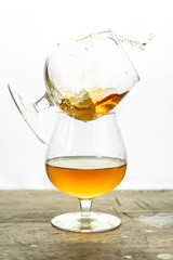 Cognac \ whiskey in cognac glass on wooden table, golden color spirits splashing on white background