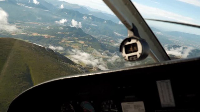 Private aircraft makes a turn, cabin view. Flying high above mountains, clouds. Driving small aeroplane above rocks, cliff, green hills in summer. Fantastic picturesque panorama