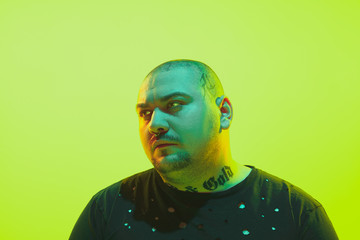Portrait of a guy with colorful neon light on green studio background. Male model with calm and serious mood. Facial expression, cyberpunk, millenials lifestyle and look like. Future, technologies.