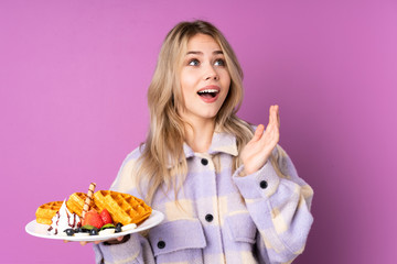 Teenager Russian girl holding waffles isolated on purple background with surprise facial expression