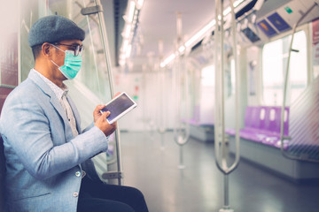 Naklejka na ściany i meble An Asian passenger with a mask to protect CoVid - 19, with a tablet on the train.