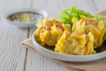 Chinese Steamed Dumpling, Shumai on white dish served with soy sauce and .lettuce leaves on brown cloth and wooden table. Delicious Dimsum pork.