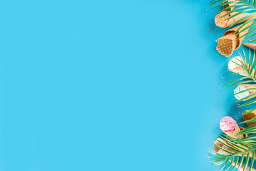 Set of various bright multicolored ice-cream in ice cream waffle cones - chocolate vanilla blueberry strawberry pistachio orange, on trendy turquoise background with summer tropical palm leaves