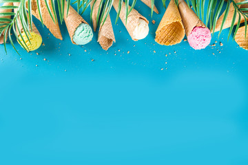 Set of various bright multicolored ice-cream in ice cream waffle cones - chocolate vanilla blueberry strawberry pistachio orange, on trendy turquoise background with summer tropical palm leaves