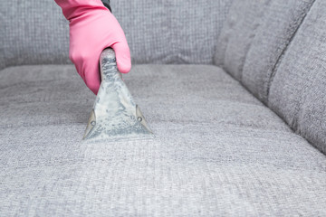 Employee hand cleaning dirty sofa with professionally extraction method. Textile upholstered...