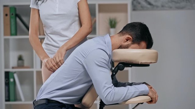 partial view of masseuse making back massage to businessman in massage chair