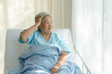 Asian elderly woman alzheimer patient sitting on the bed and look outside window at home.