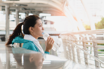 Woman drinking water during jogging break in the morning to protect dehydrate and heat strokes.