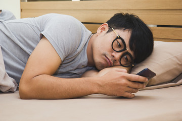 Bored asian male using smartphone on the bed in the midnight. - Powered by Adobe
