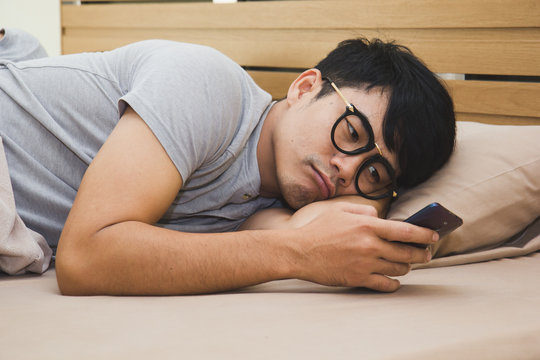 Bored asian male using smartphone on the bed in the midnight.