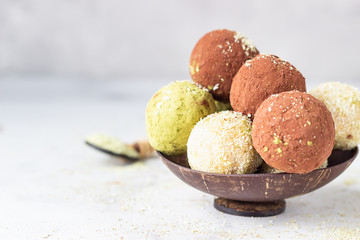 Homemade raw energy balls with matcha tea powder, cocoa powder and coconut flakes in a wooden bowl, light grey background. Selective focus. Vegan sweets. 