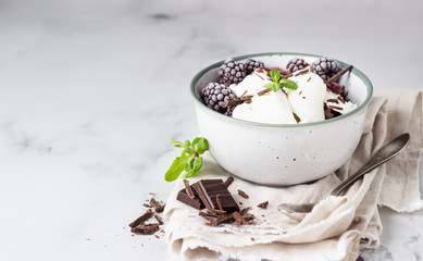 Vanilla ice cream with frozen raspberries, blackberries, chocolate and mint in a ceramic bowl, light grey background.