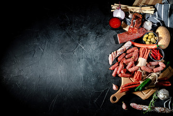 Different kinds of delicious smoked dried sausages, salami or kabanos on dark background