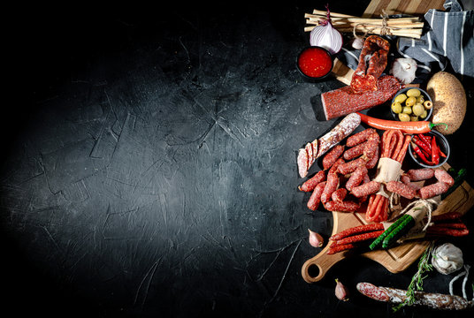 Different kinds of delicious smoked dried sausages, salami or kabanos on dark background