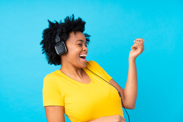 Young african american woman listening music with a mobile over isolated blue wall