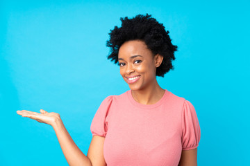 African american woman over isolated blue background holding copyspace imaginary on the palm
