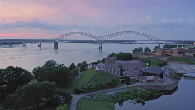Aerial flying Mud Island River Park to the Hernando de Soto Bridge crossing the Mississippi River at sunset. The bridge crosses into Arkansas. Memphis, Tennessee, USA