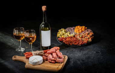 Antipasto set with gourmet food on black table top view. Mixed delicatessen of cheese and meat snacks with wine