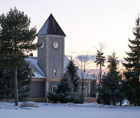 Fototapeta na wymiar A clock tower surrounded by pines and firs in winter evening.