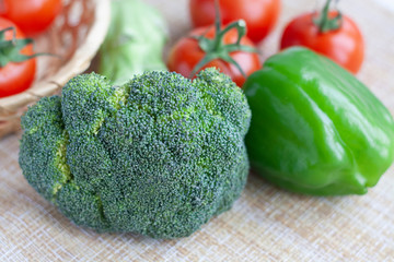 Raw broccoli, green bell peppers and tomatoes in a basket and pepper shaker