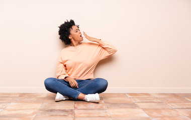 African american woman sitting on the floor yawning and covering wide open mouth with hand