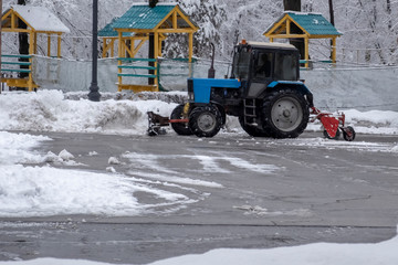 Tractor is cleaning snow in park. Tractor is sweeping snow in snowfall.