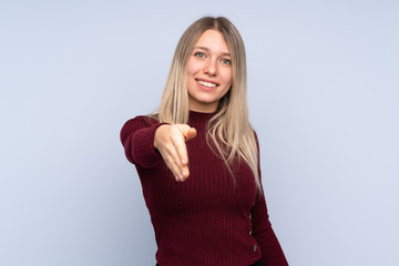 Young blonde woman over isolated blue background shaking hands for closing a good deal