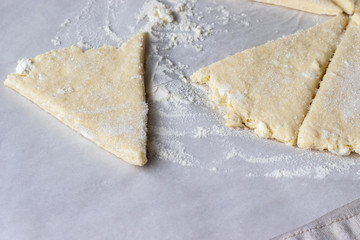 Rolled raw curd dough cut into eight triangles sprinkled with sugar and one triangle of dough lies separately on baking paper on a linen tablecloth. The process of making curd bagels or croissants