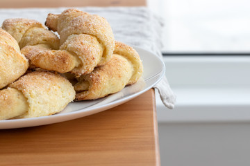 Sugar-frosted croissants from a cottage cheese dough on a white plate on a wooden table with linen tablecloth. Tea snack for breakfast. The process of making curd bagels or croissants. Selective focus
