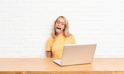young blonde woman with cheerful, carefree, rebellious attitude, joking and sticking tongue out,...