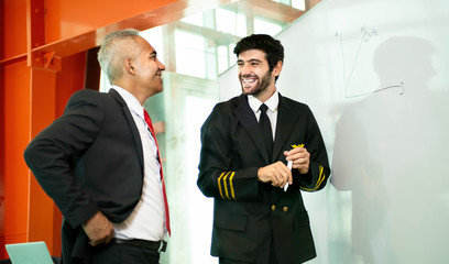 Young pilot man in uniform writing graph by marker on whiteboard having discussion with business man about aviation businessn,startup,business team,people,economics,analytics and statistics concept,