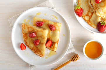 Homemade crepes with strawberry slices and honey, tasty breakfast