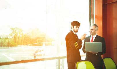 Business caucasian man in suit and young pilot man in uniform standing and using laptop talking...
