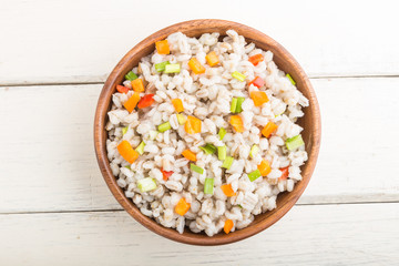 Pearl barley porridge with vegetables in wooden bowl on a white wooden background. Top view, close up.
