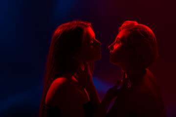 Two young beautiful women in lingerie posing in red back light