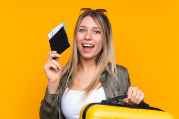 Young blonde woman over isolated yellow background in vacation with suitcase and passport