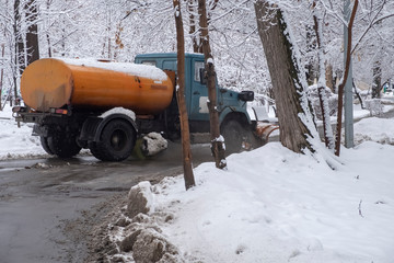 Truck is cleaning snow in park after snowfall. Snow blizzard snowstorm background. Industrial...