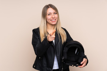 Young blonde woman with a motorcycle helmet over isolated background points finger at you