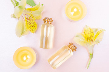 The concept of aromatherapy, spa. Bottles with floral essential oil, a yellow flower and candles on a pastel pink background. Cozy flat lay in bright colors. Copyspace, minimalism, top view.